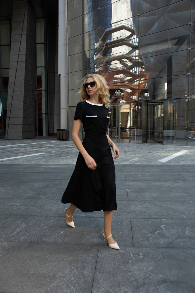 Side view of black midi dress with contrasting white trim on the collar and pockets.