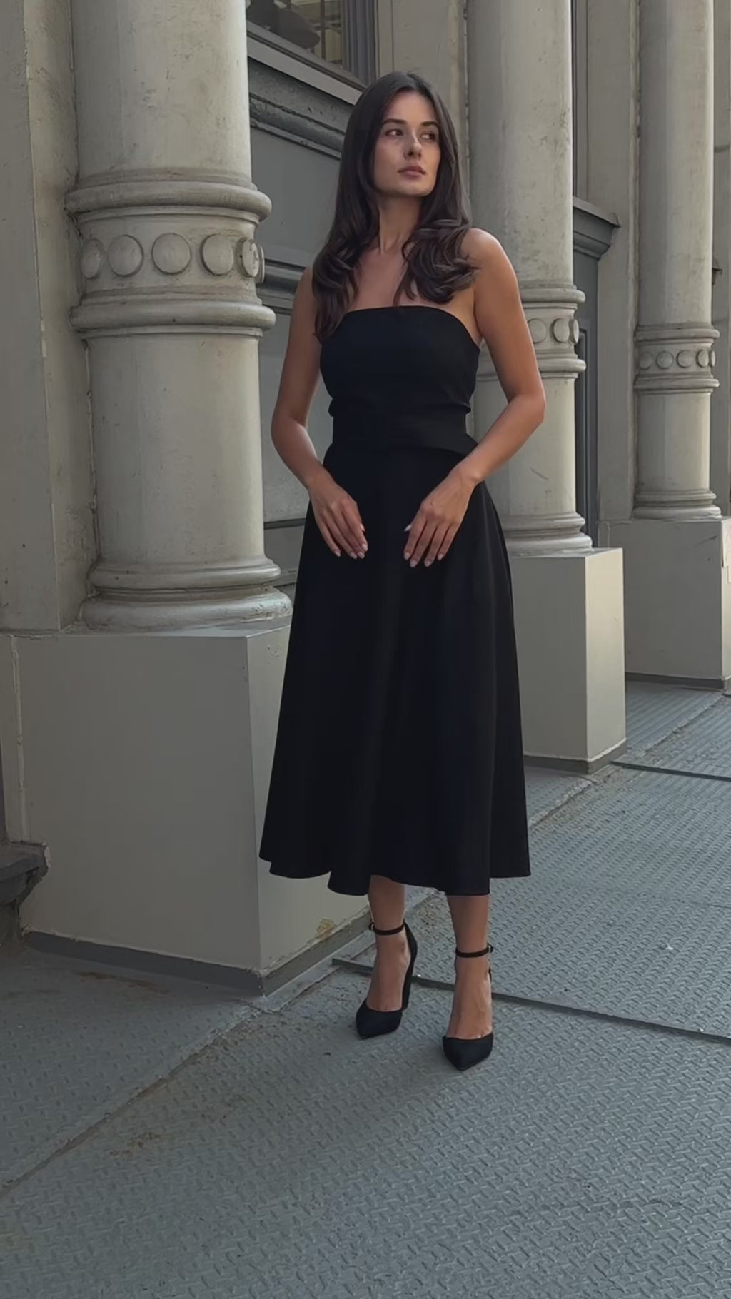 A confident woman walking in New York City wearing an elegant black strapless cocktail dress by Anastasiia Ivanova. The tailored A-line silhouette makes it the perfect wedding guest or black tie outfit