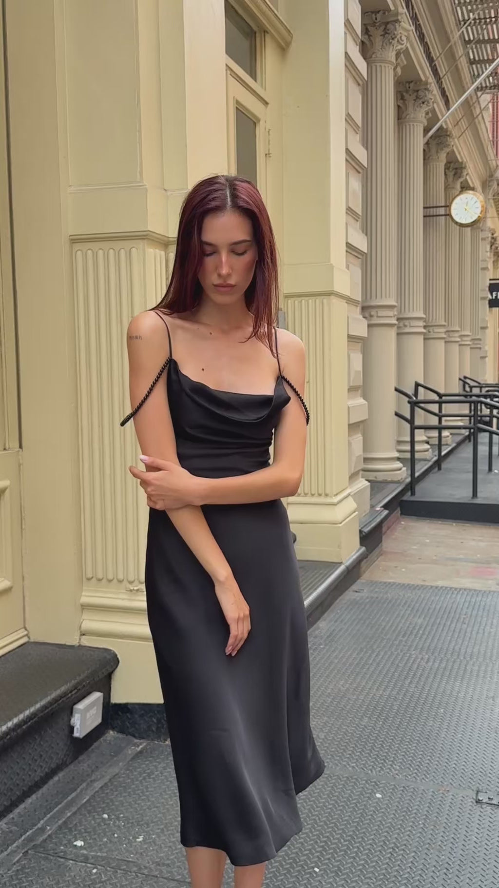 Lifestyle video of a woman walking through the city in a black silk pearl strap midi dress, showcasing the fluid motion and elegant drape of the formal evening gown.