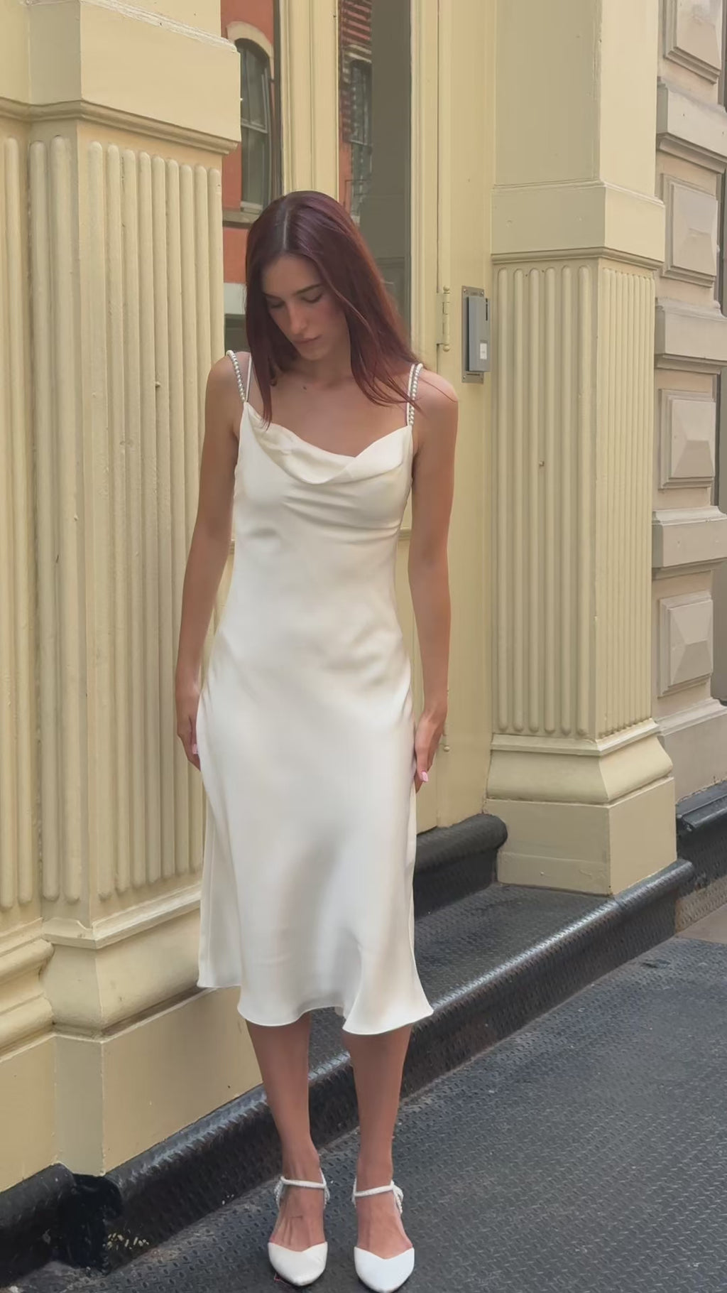 Dynamic lifestyle video of a bride walking in the city wearing an ivory silk pearl strap midi dress, highlighting the luxurious bias-cut drape and movement