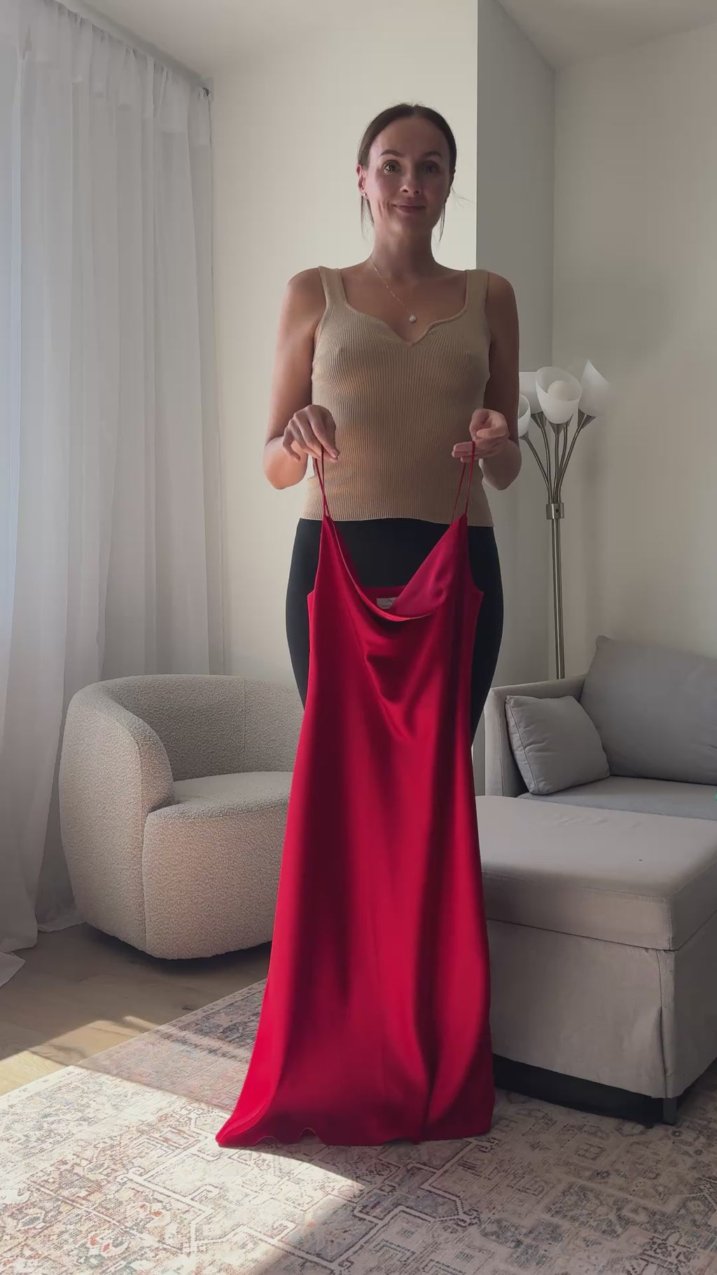 Woman trying on a luxurious red silk slip dress at home in front of a mirror. Showcasing the flawless bias-cut fit, elegant drape, and vibrant color, perfect for a romantic date night or formal evening event