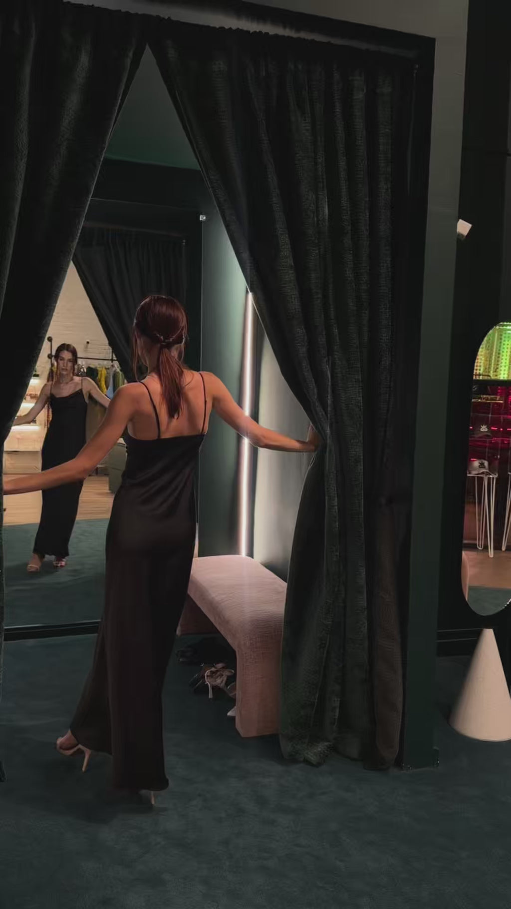 Close-up fitting video of a formal black silk maxi slip dress in a mirror, highlighting the impeccable seams, adjustable spaghetti straps, and elegant cowl neckline