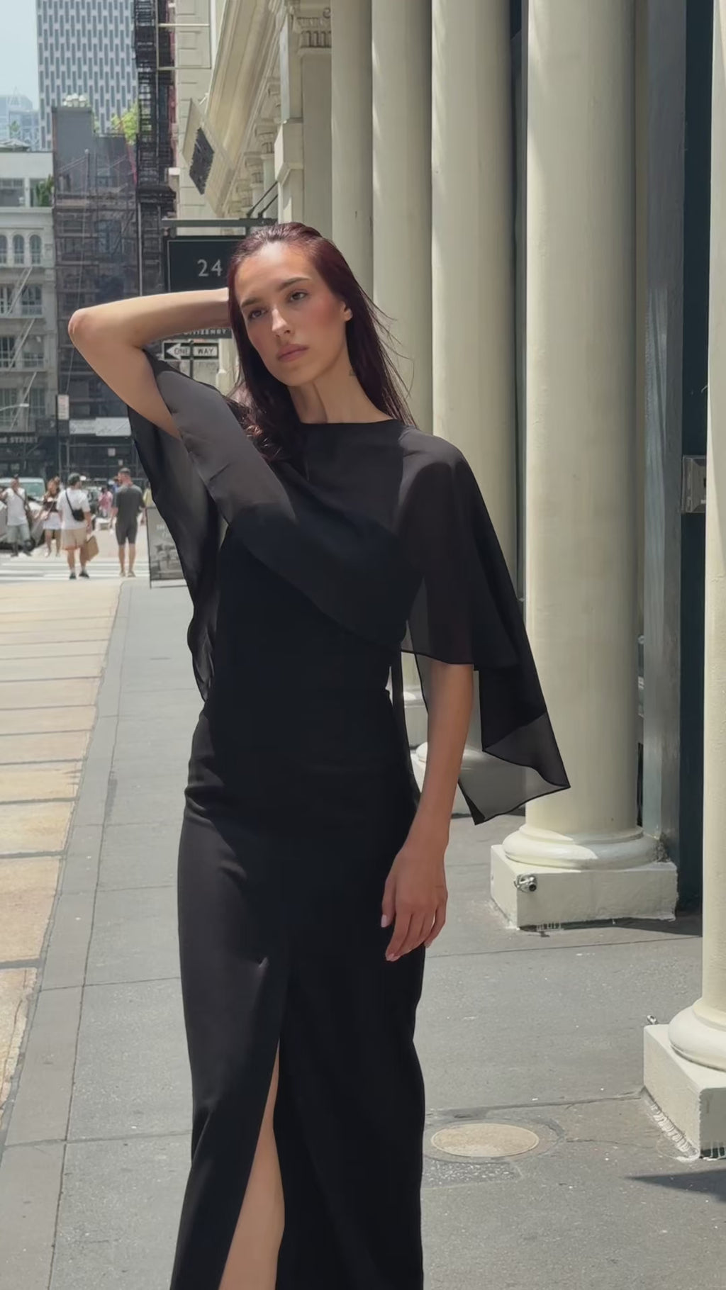 Dynamic video of a woman walking in the city wearing a luxury black strapless maxi dress styled with a sheer chiffon capelet. Showcasing the elegant movement, flawless fit, and romantic drape for a formal evening or black-tie event.