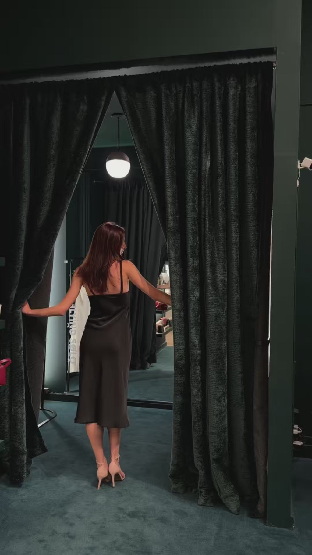 Close-up fitting video of a black silk formal slip dress in a mirror, highlighting the impeccable tailoring, adjustable strap, and draped black ceramic pearl details.